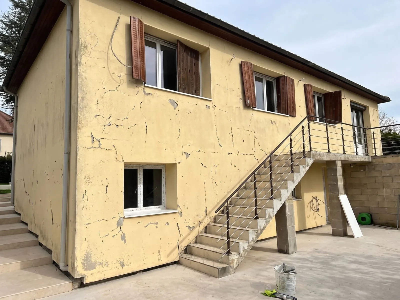 Pignon de pavillon en enduit jaune fissuré et cloqué par endroits, avant travaux.