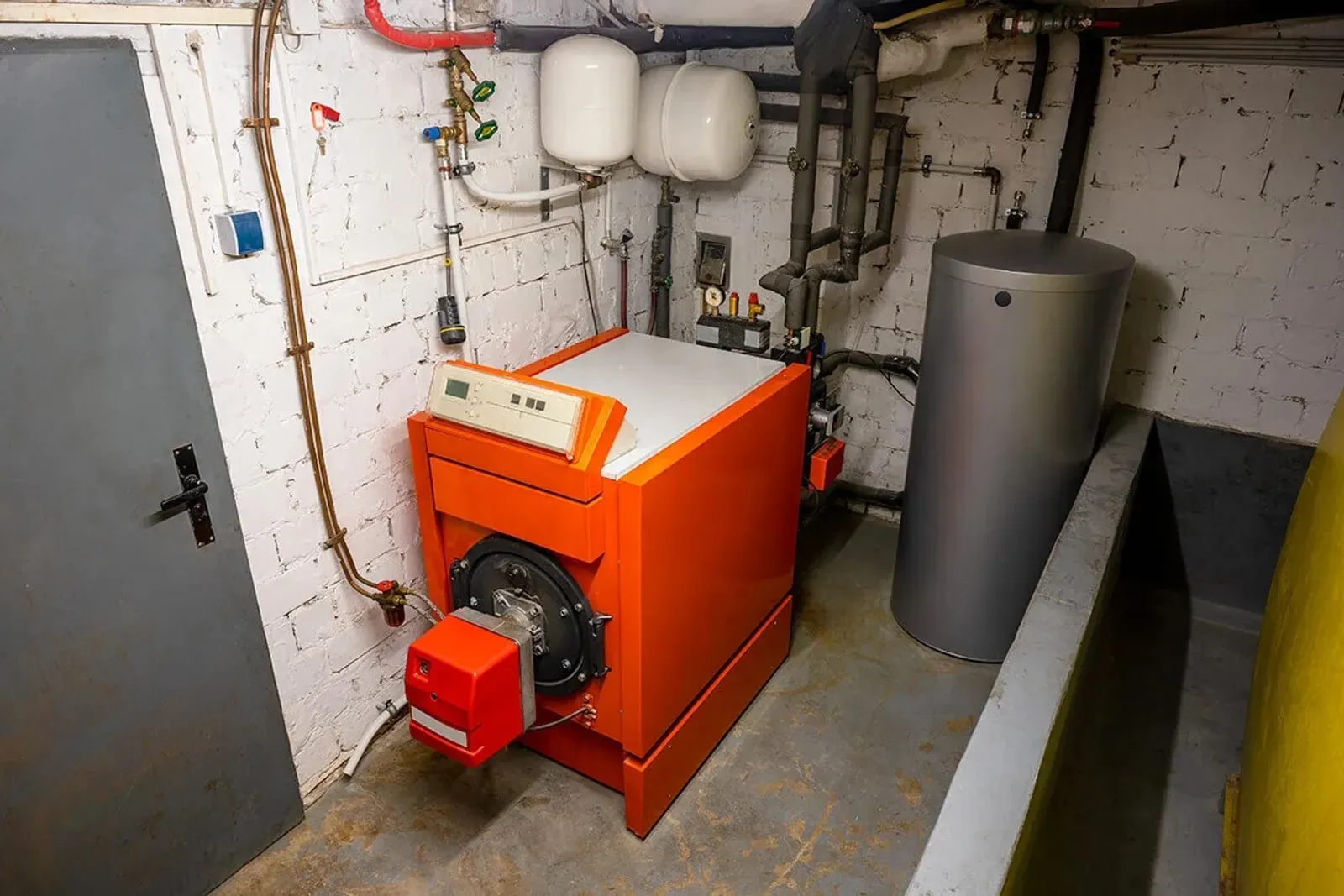 Chaufferie de sous-sol équipée d'une chaudière fioul orange et de son ballon, avant travaux.